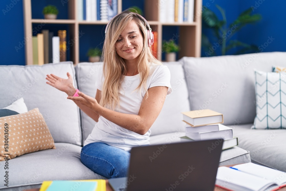 Young blonde woman studying using computer laptop at home inviting to enter smiling natural with open hand Young blonde woman studying using computer laptop at home inviting to enter smiling natural with open hand