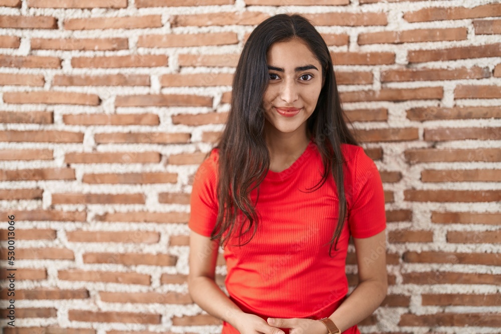Young teenager girl standing over bricks wall with hands together and crossed fingers smiling relaxed and cheerful. success and optimistic Young teenager girl standing over bricks wall with hands together and crossed fingers smiling relaxed and cheerful. success and optimistic