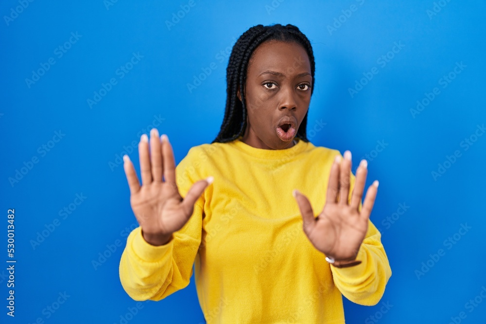 Beautiful black woman standing over blue background moving away hands palms showing refusal and denial with afraid and disgusting expression. stop and forbidden. Beautiful black woman standing over blue background moving away hands palms showing refusal and denial with afraid and disgusting expression. stop and forbidden.