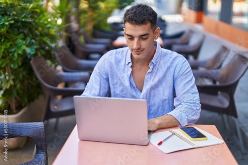 Young hispanic man using laptop sitting on table at coffee shop terrace © Krakenimages.com