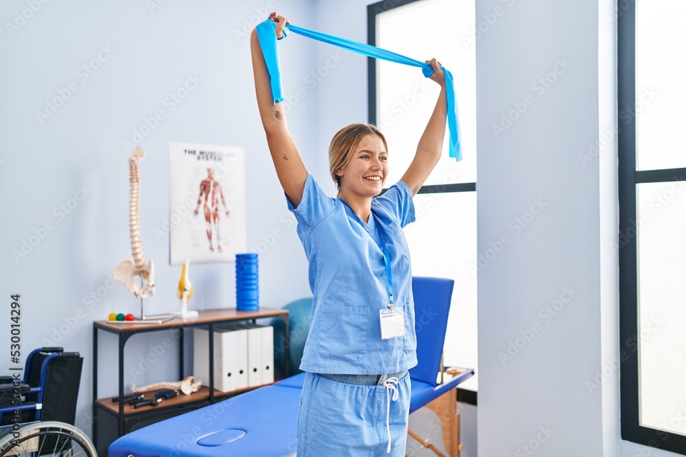 Young hispanic woman physiotherapist stretching arms using elastic band at rehab clinic Young hispanic woman physiotherapist stretching arms using elastic band at rehab clinic