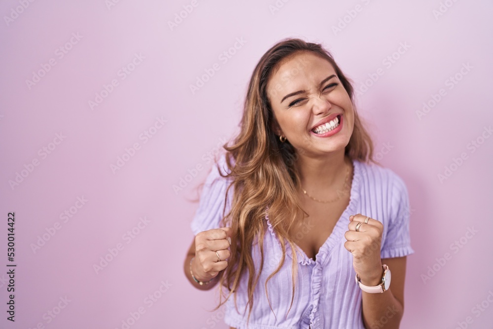 Young hispanic woman standing over pink background very happy and excited doing winner gesture with arms raised, smiling and screaming for success. celebration concept. Young hispanic woman standing over pink background very happy and excited doing winner gesture with arms raised, smiling and screaming for success. celebration concept.