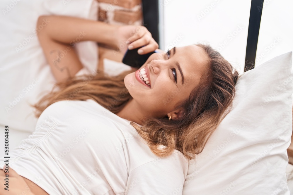 Fototapeta premium Young beautiful hispanic woman talking on smartphone lying on bed at bedroom