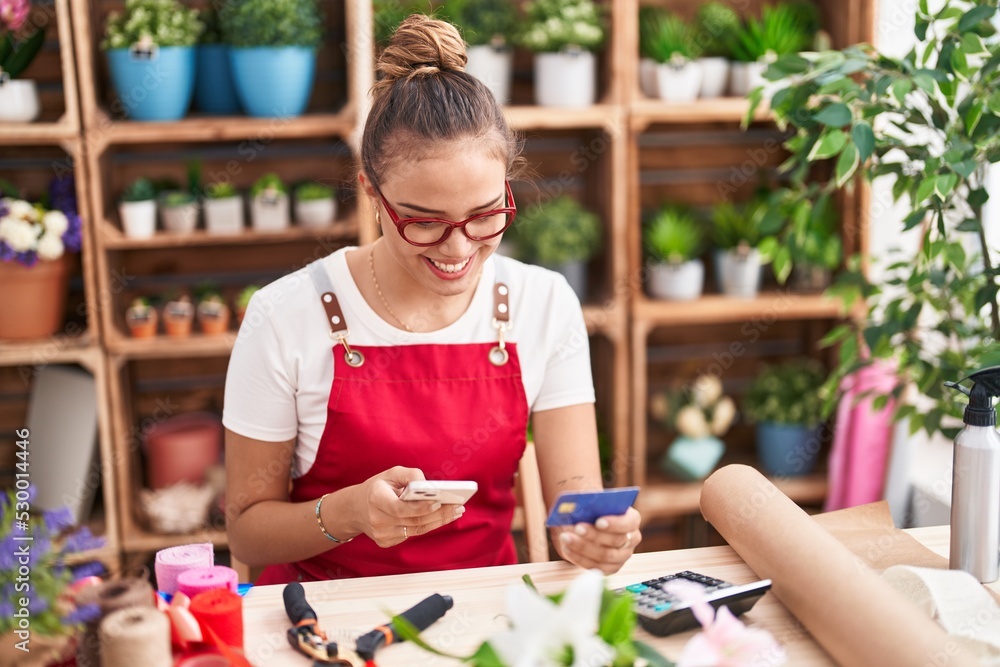 Fototapeta premium Young beautiful hispanic woman florist using smartphone and credit card at florist
