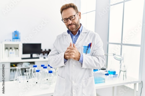 Middle age hispanic man wearing scientist uniform standing at laboratory