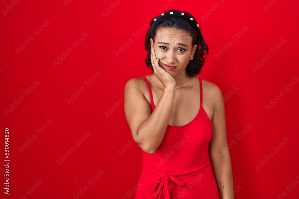 Young hispanic woman standing over red background touching mouth with hand with painful expression because of toothache or dental illness on teeth. dentist Young hispanic woman standing over red background touching mouth with hand with painful expression because of toothache or dental illness on teeth. dentist