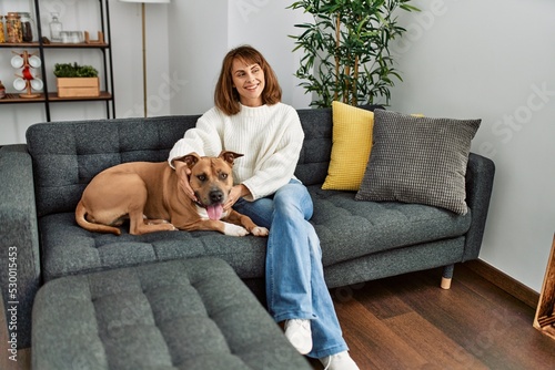 Young caucasian woman smiling confident hugging dog sitting on sofa at home
