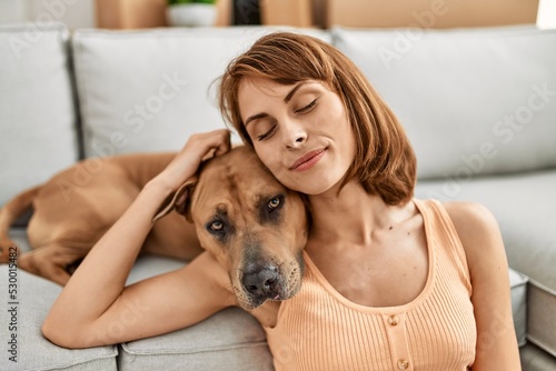 Young caucasian woman hugging dog sitting on floor at home