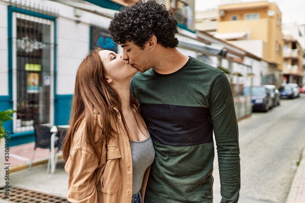 Young interracial couple kissing and hugging standing at the city.