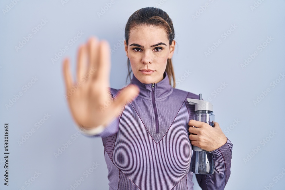 Beautiful woman wearing sportswear holding water bottle doing stop sing with palm of the hand. warning expression with negative and serious gesture on the face. Beautiful woman wearing sportswear holding water bottle doing stop sing with palm of the hand. warning expression with negative and serious gesture on the face.