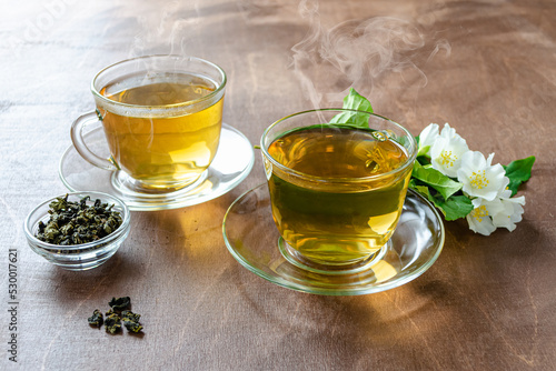 two cups of jasmine tea and brewing on a wooden table next to sprigs of jasmine with leaves and flowers, herbal tea medicinal dietary