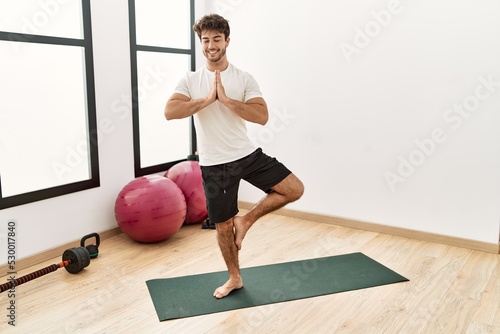 Young hispanic man smiling confident training yoga exercise at sport center