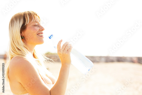 Photos Beautiful woman drinks water. Young happy woman at the beach.