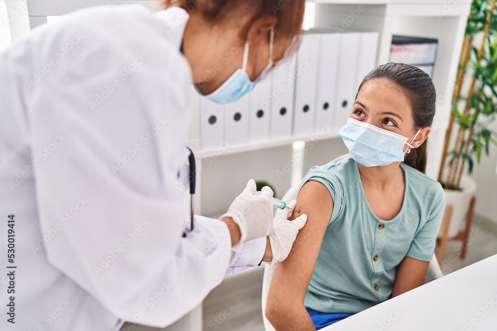 Woman and girl doctor and patient wearing medical mask vaccinating arm at clinic Woman and girl doctor and patient wearing medical mask vaccinating arm at clinic