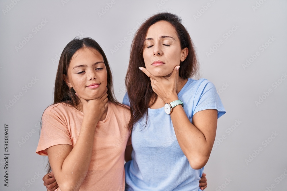 Young mother and daughter standing over white background touching painful neck, sore throat for flu, clod and infection Young mother and daughter standing over white background touching painful neck, sore throat for flu, clod and infection