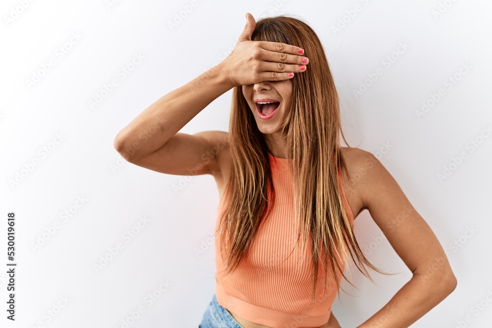 Hispanic woman with bang hairstyle standing over isolated background smiling and laughing with hand on face covering eyes for surprise. blind concept. Hispanic woman with bang hairstyle standing over isolated background smiling and laughing with hand on face covering eyes for surprise. blind concept.