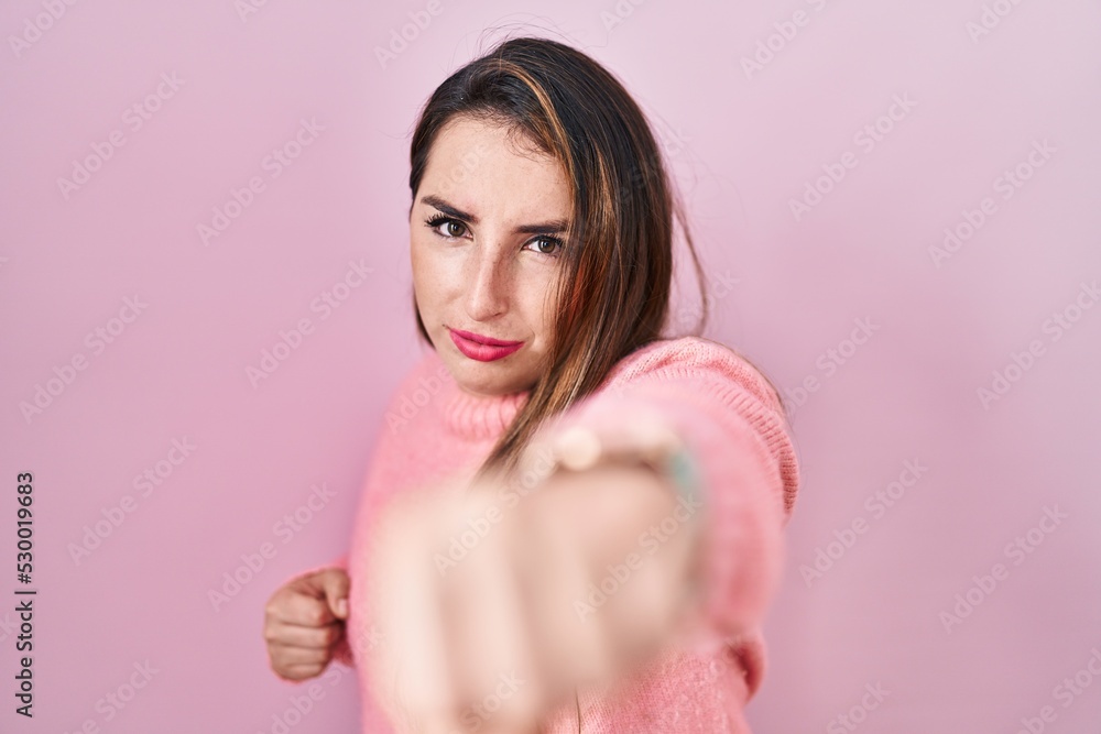 Young hispanic woman standing over pink background punching fist to fight, aggressive and angry attack, threat and violence Young hispanic woman standing over pink background punching fist to fight, aggressive and angry attack, threat and violence