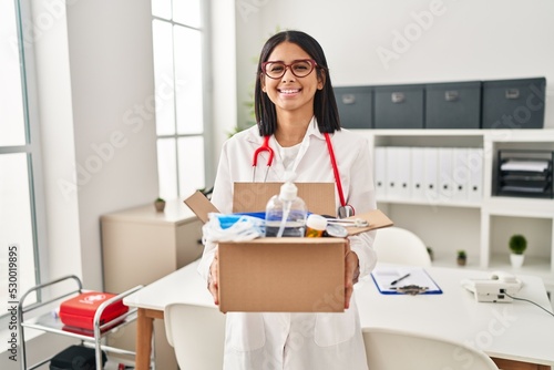 Young hispanic doctor woman holding box with medical items smiling with a happy and cool smile on face. showing teeth.
