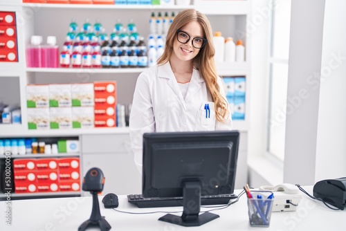 Young woman pharmacist smiling confident using computer at pharmacy