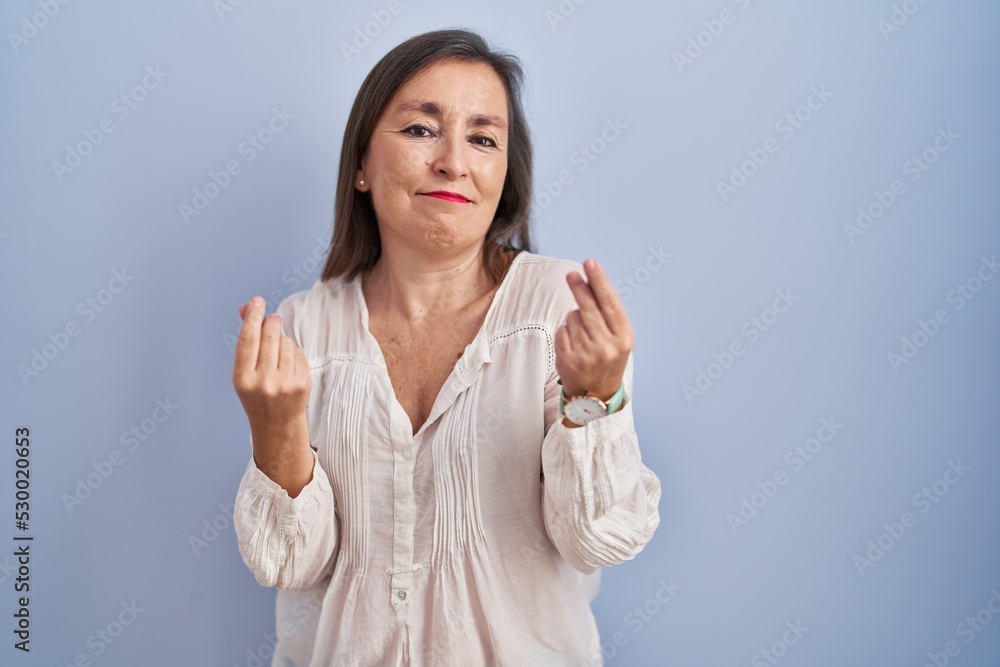 Middle age hispanic woman standing over blue background doing money gesture with hands, asking for salary payment, millionaire business Middle age hispanic woman standing over blue background doing money gesture with hands, asking for salary payment, millionaire business