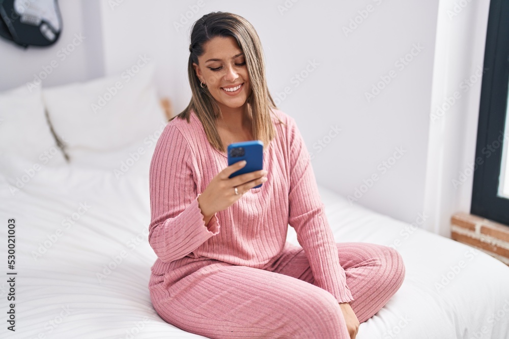 Young hispanic woman using smartphone sitting on bed at bedroom Young hispanic woman using smartphone sitting on bed at bedroom