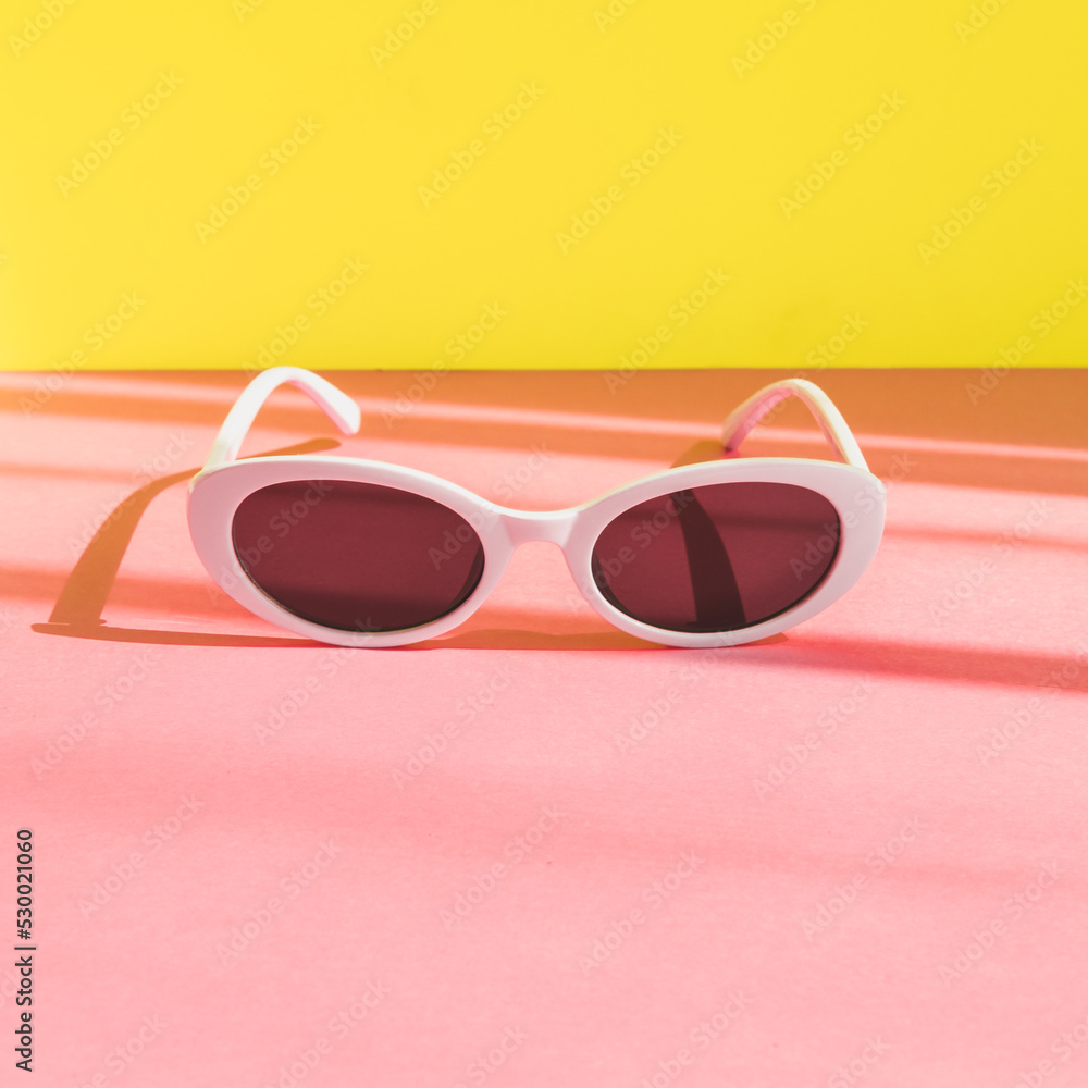 women's sunglasses in a white frame on a yellow and pink background. minimalism and pop art style. women's sunglasses in a white frame on a yellow and pink background. minimalism and pop art style.