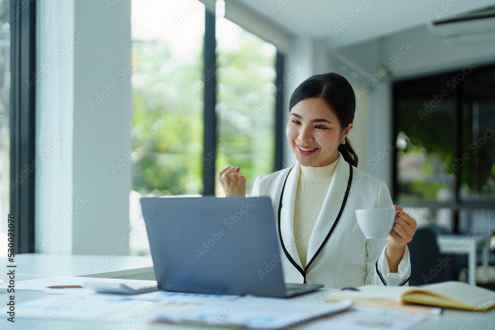 young Asian woman using a computer showing joy at the sales target.