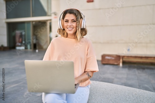 Young hispanic woman smiling confident using laptop and headphones at street