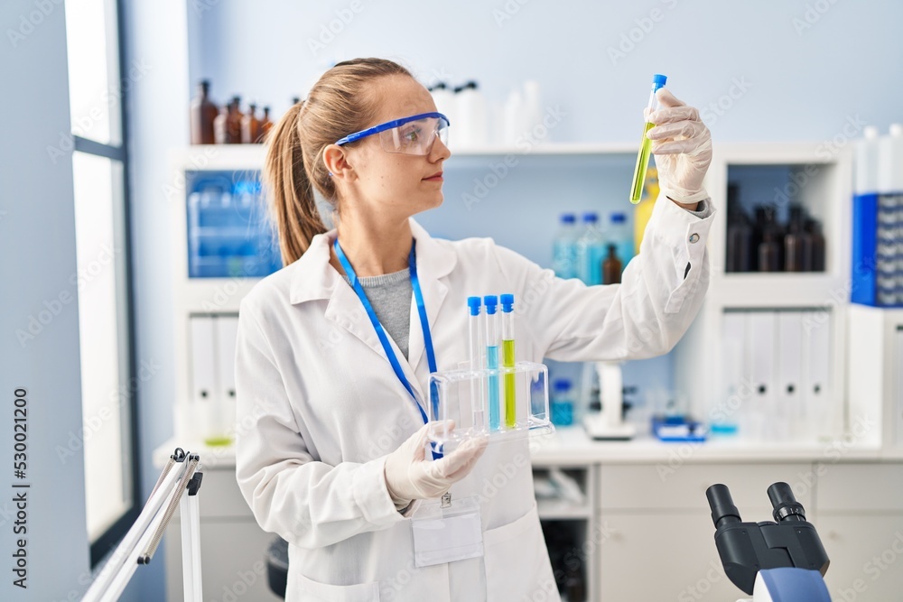 Fototapeta premium Young blonde woman wearing scientist uniform holding test tube at laboratory