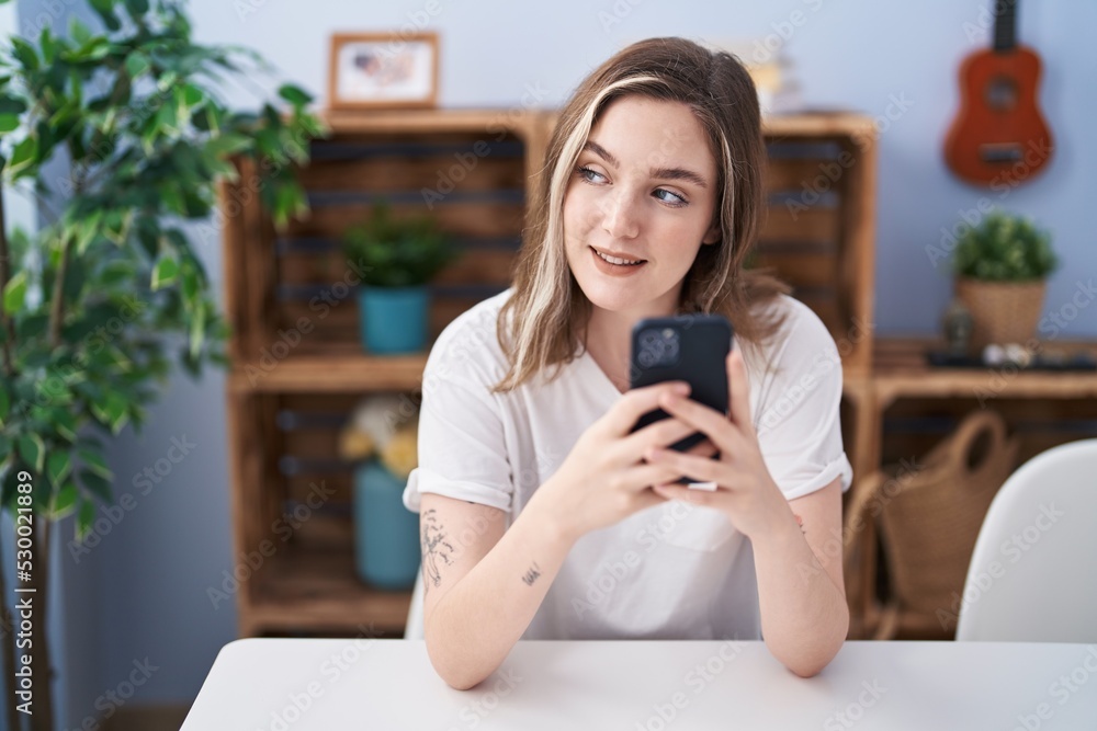 Young woman using smartphone sitting on table at home Young woman using smartphone sitting on table at home