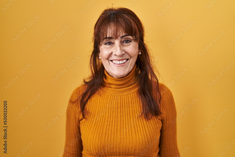Middle age hispanic woman standing over yellow background with a happy and cool smile on face. lucky person. Middle age hispanic woman standing over yellow background with a happy and cool smile on face. lucky person.