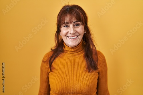 Middle age hispanic woman standing over yellow background with a happy and cool smile on face. lucky person. © Krakenimages.com