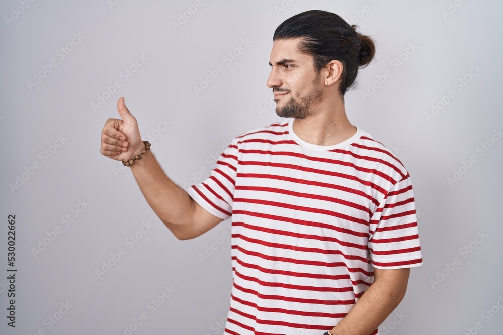 Hispanic man with long hair standing over isolated background looking proud, smiling doing thumbs up gesture to the side Hispanic man with long hair standing over isolated background looking proud, smiling doing thumbs up gesture to the side