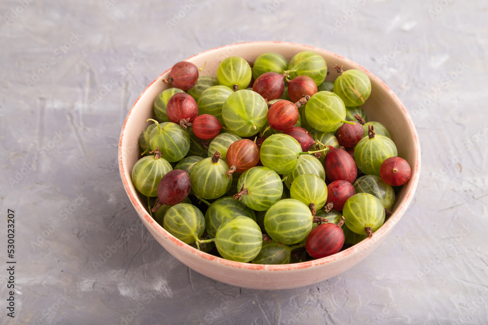 Fresh red and green gooseberry in ceramic bowl on gray concrete, side view. Fresh red and green gooseberry in ceramic bowl on gray concrete, side view.