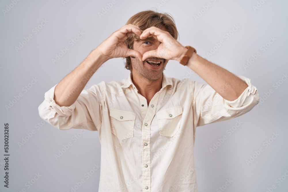 Middle age man standing over isolated background doing heart shape with hand and fingers smiling looking through sign Middle age man standing over isolated background doing heart shape with hand and fingers smiling looking through sign