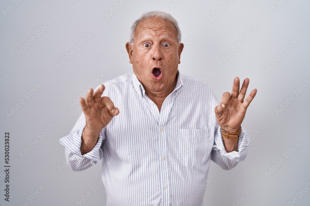 Senior man with grey hair standing over isolated background looking surprised and shocked doing ok approval symbol with fingers. crazy expression Senior man with grey hair standing over isolated background looking surprised and shocked doing ok approval symbol with fingers. crazy expression
