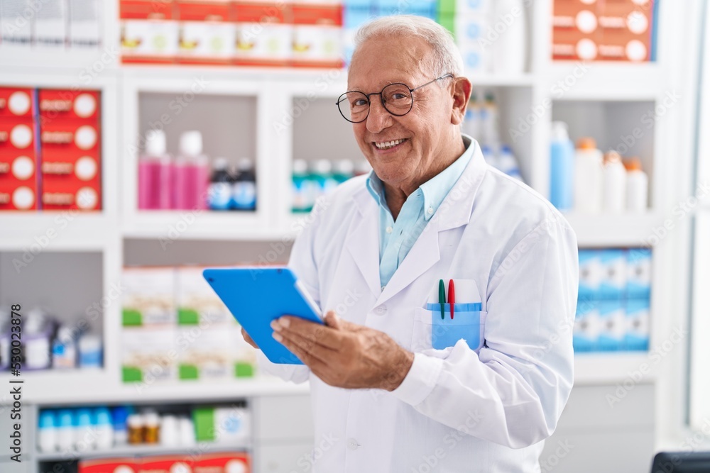 Senior grey-haired man pharmacist using touchpad at pharmacy Senior grey-haired man pharmacist using touchpad at pharmacy