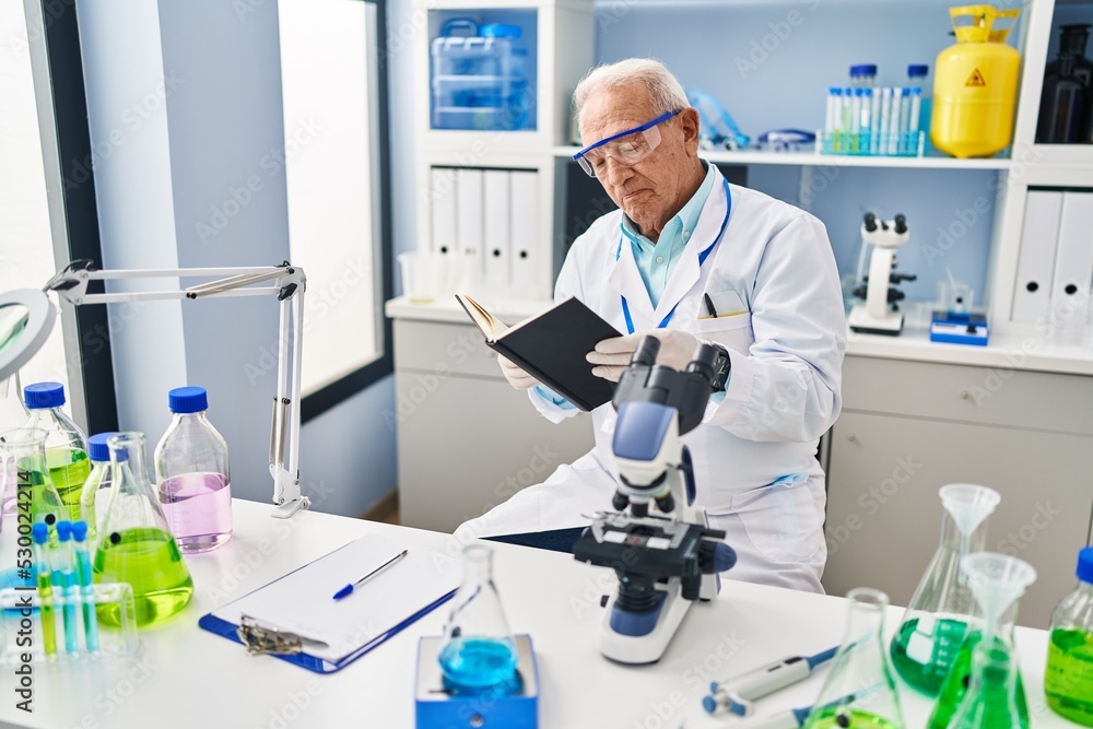 Senior man wearing scientist uniform reading book at laboratory Senior man wearing scientist uniform reading book at laboratory