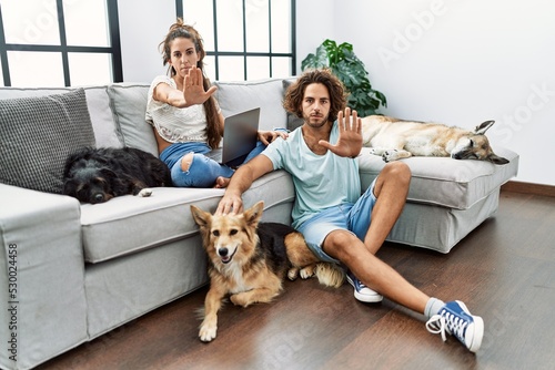 Young hispanic couple with dogs relaxing at home doing stop sing with palm of the hand. warning expression with negative and serious gesture on the face. © Krakenimages.com
