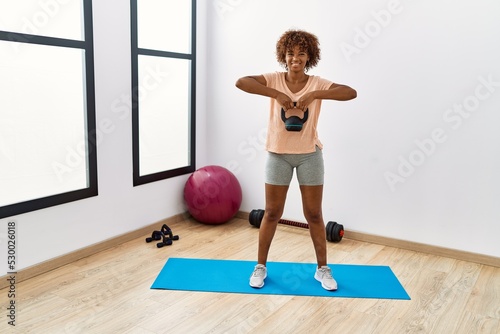 Young african american woman smiling confident training using ketlebell at sport center