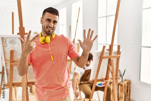 Young hispanic man at art studio showing and pointing up with fingers number eight while smiling confident and happy.