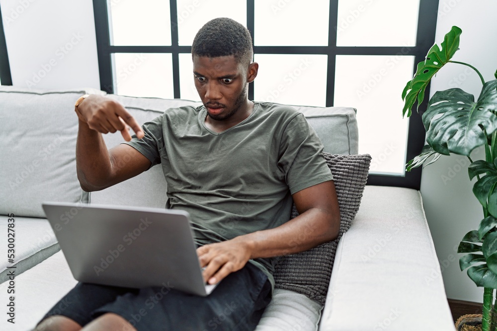 Young african american man using laptop at home sitting on the sofa ...