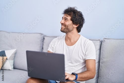 Young hispanic man using laptop sitting on sofa at home