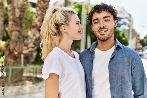 Young beautiful couple of caucasian girlfriend and hispanic boyfriend hugging in love outdoors on a sunny day. Woman and man smiling happy dating relationship