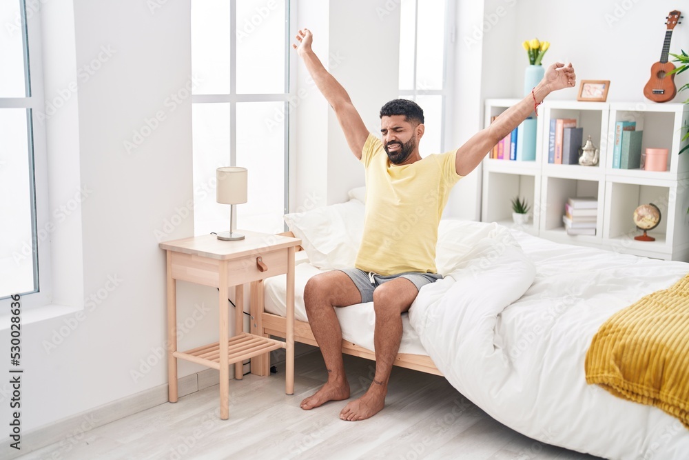 Young arab man waking up stretching arms at bedroom Young arab man waking up stretching arms at bedroom