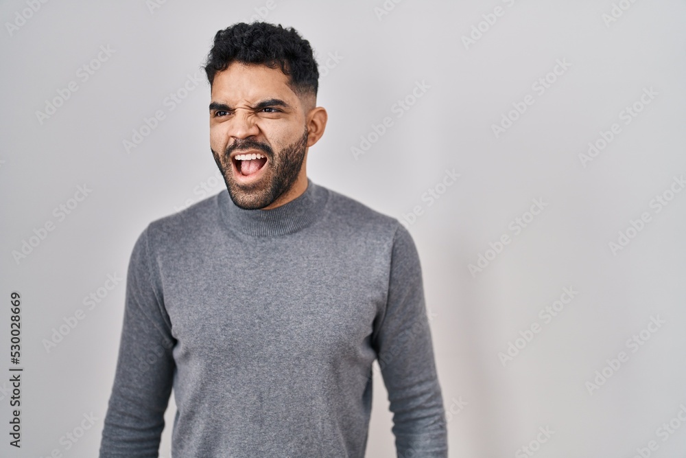 Hispanic man with beard standing over white background angry and mad screaming frustrated and furious, shouting with anger. rage and aggressive concept. Hispanic man with beard standing over white background angry and mad screaming frustrated and furious, shouting with anger. rage and aggressive concept.