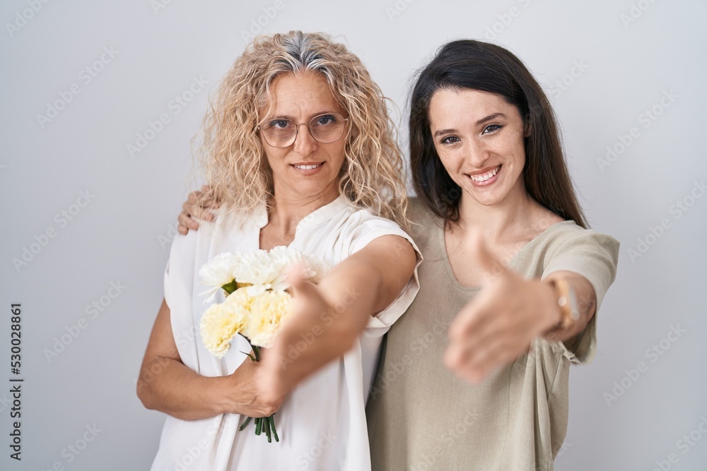 Obraz premium Mother and daughter holding bouquet of white flowers smiling friendly offering handshake as greeting and welcoming. successful business.