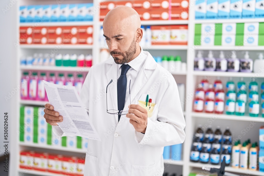 Young bald man pharmacist reading prescription at pharmacy Young bald man pharmacist reading prescription at pharmacy