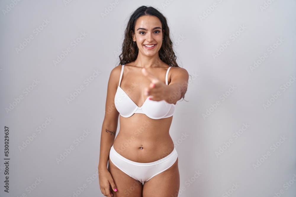 Fototapeta premium Young hispanic woman wearing white lingerie smiling friendly offering handshake as greeting and welcoming. successful business.