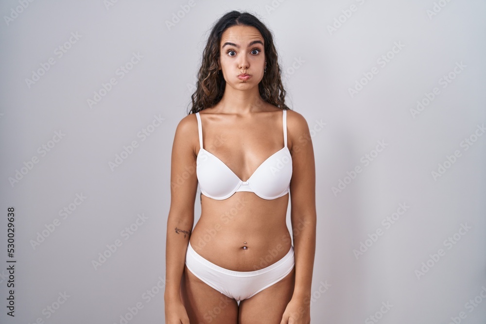 Young hispanic woman wearing white lingerie puffing cheeks with funny face. mouth inflated with air, crazy expression. Young hispanic woman wearing white lingerie puffing cheeks with funny face. mouth inflated with air, crazy expression.